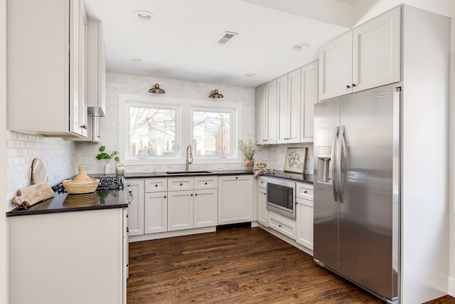 kitchen featuring dark countertops, visible vents, appliances with stainless steel finishes, white cabinetry, and a sink