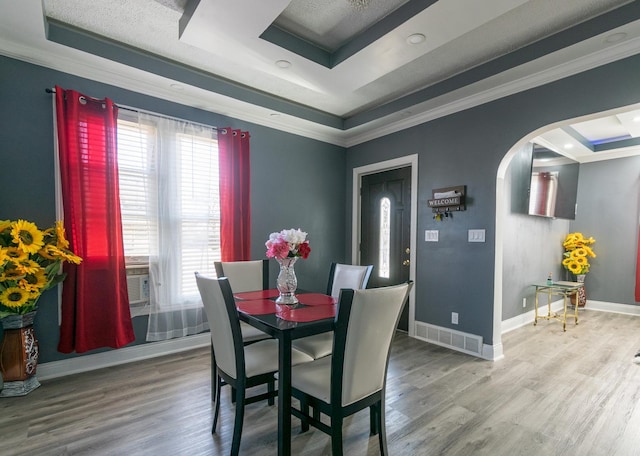 dining area with arched walkways, a raised ceiling, crown molding, and wood finished floors