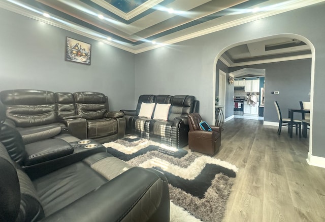 home theater room featuring baseboards, arched walkways, a raised ceiling, wood finished floors, and crown molding