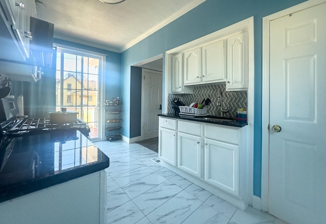 kitchen featuring baseboards, decorative backsplash, marble finish floor, crown molding, and white cabinetry