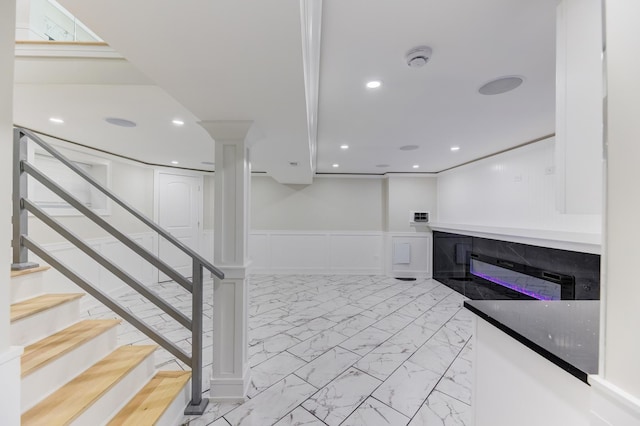 interior space featuring marble finish floor, recessed lighting, a decorative wall, a glass covered fireplace, and wainscoting