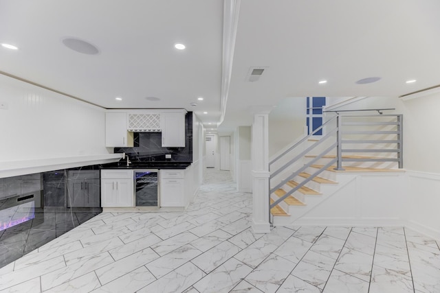 kitchen with dark countertops, beverage cooler, white cabinets, and marble finish floor