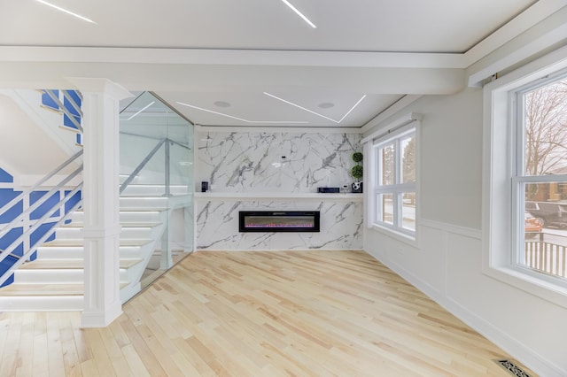 unfurnished living room featuring a fireplace, visible vents, wainscoting, wood finished floors, and stairs