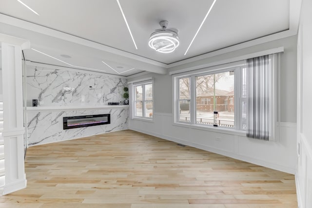 unfurnished living room featuring light wood-type flooring, a wainscoted wall, a fireplace, and a decorative wall