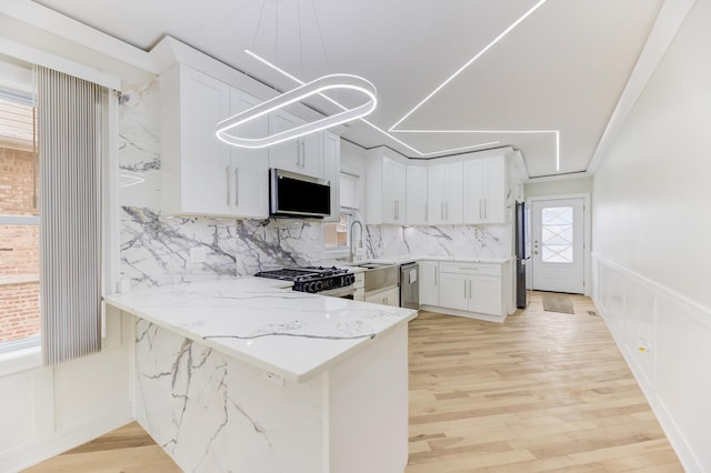 kitchen with stove, white cabinetry, light stone countertops, light wood-type flooring, and a peninsula