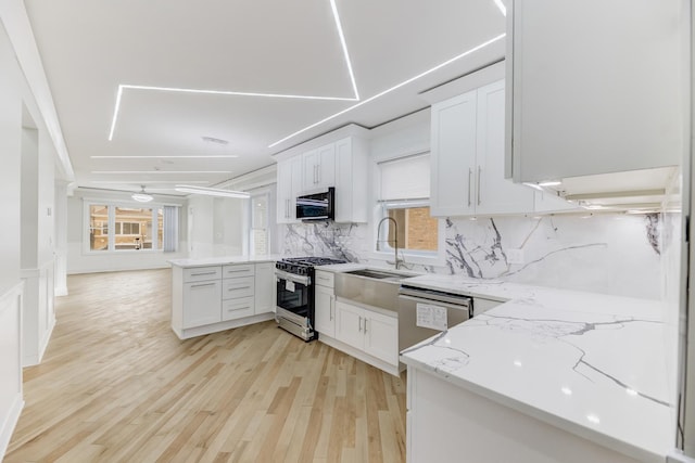 kitchen featuring white cabinets, light stone countertops, stainless steel appliances, light wood-style floors, and a sink