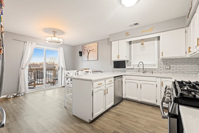 kitchen with stainless steel appliances, white cabinets, a sink, and a peninsula