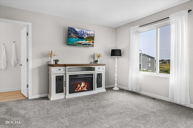 unfurnished living room featuring a warm lit fireplace, carpet, and baseboards