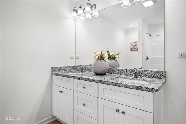 bathroom featuring a shower, a sink, baseboards, and double vanity