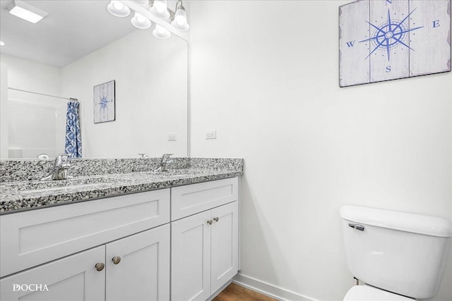 bathroom with double vanity, baseboards, a shower with shower curtain, toilet, and a sink