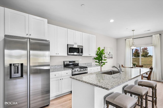 kitchen with light stone countertops, a center island with sink, stainless steel appliances, and a sink