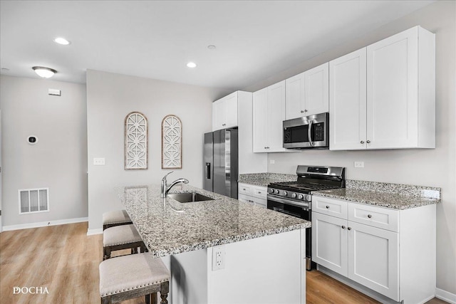 kitchen with visible vents, appliances with stainless steel finishes, light stone countertops, a kitchen island with sink, and a sink