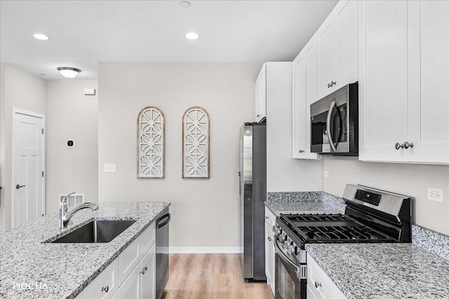 kitchen with a sink, white cabinetry, light wood-style floors, appliances with stainless steel finishes, and light stone countertops