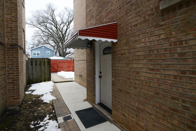 snow covered property entrance with brick siding and fence