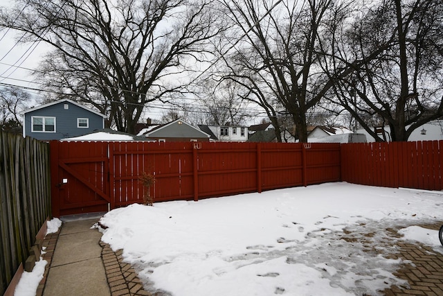 snowy yard with a fenced backyard and a gate