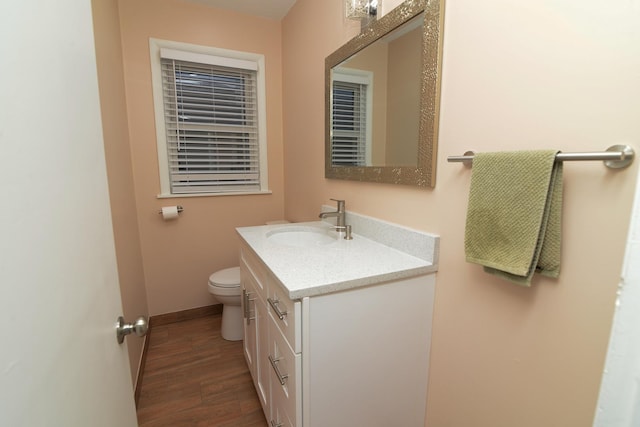 half bathroom with toilet, wood finished floors, vanity, and baseboards