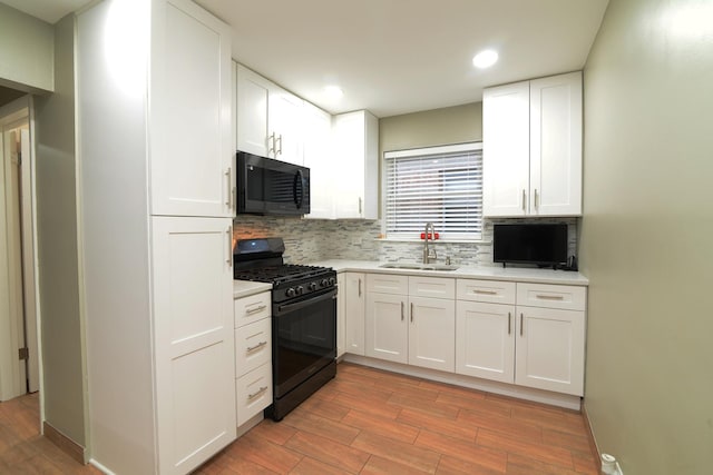 kitchen with black range with gas cooktop, a sink, white cabinetry, light countertops, and tasteful backsplash