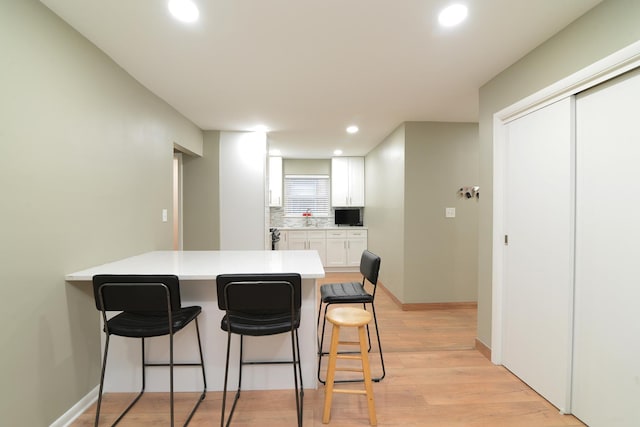 kitchen with a breakfast bar, white cabinetry, light countertops, light wood-type flooring, and tasteful backsplash