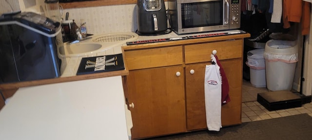 kitchen featuring wallpapered walls, stainless steel microwave, and brown cabinets