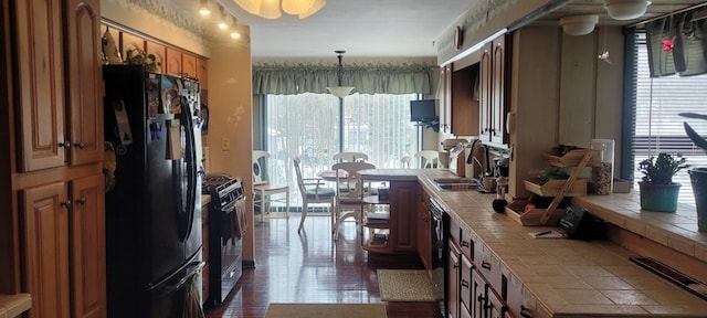 kitchen with decorative light fixtures, tile countertops, brown cabinetry, a sink, and black appliances