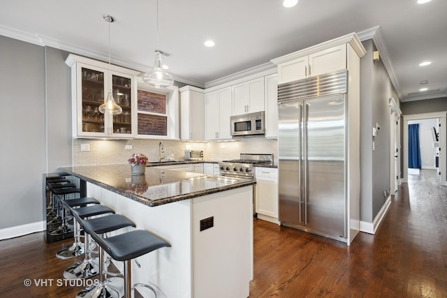 kitchen featuring white cabinets, premium appliances, glass insert cabinets, a kitchen breakfast bar, and pendant lighting