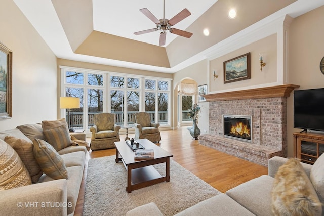 living area with ceiling fan, arched walkways, light wood-style flooring, a high ceiling, and a fireplace