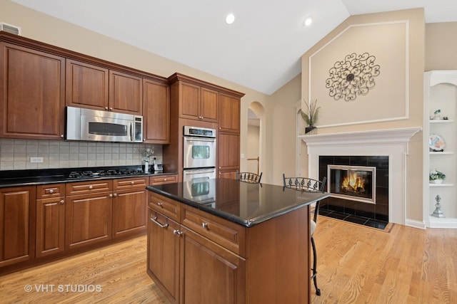 kitchen with light wood-style flooring, vaulted ceiling, stainless steel appliances, and a tile fireplace