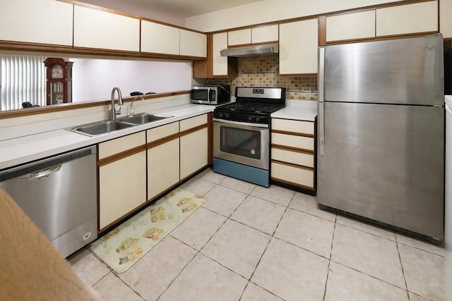 kitchen with light tile patterned flooring, under cabinet range hood, a sink, light countertops, and appliances with stainless steel finishes