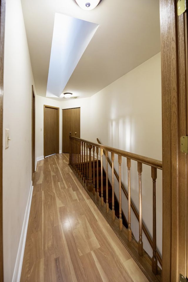 corridor featuring light wood finished floors, baseboards, and an upstairs landing