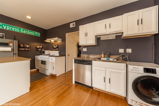 kitchen with dark countertops, appliances with stainless steel finishes, washer / clothes dryer, and white cabinets