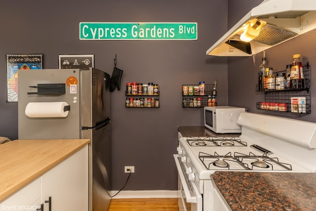 kitchen featuring white appliances, light wood-style floors, white cabinets, dark countertops, and island exhaust hood