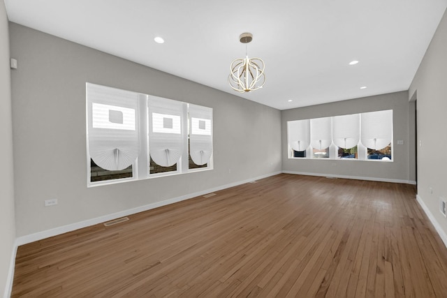 unfurnished living room with baseboards, wood-type flooring, visible vents, and an inviting chandelier