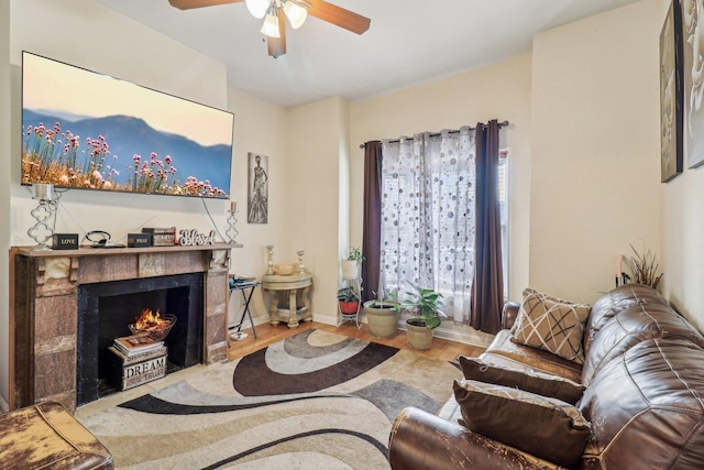 living room with a warm lit fireplace, wood finished floors, a ceiling fan, and baseboards