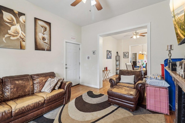 living room featuring baseboards, wood finished floors, and ceiling fan with notable chandelier