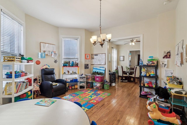 game room with ceiling fan with notable chandelier and hardwood / wood-style flooring