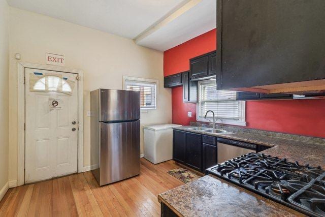 kitchen with baseboards, appliances with stainless steel finishes, a sink, and light wood-style floors