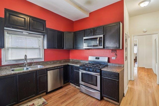 kitchen featuring stainless steel appliances, dark countertops, a sink, and light wood-style flooring