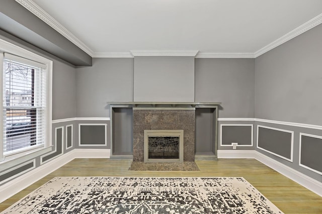 unfurnished living room featuring ornamental molding, a premium fireplace, wood finished floors, and a decorative wall