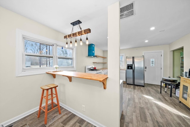 kitchen featuring stainless steel fridge, visible vents, a breakfast bar, and wood finished floors