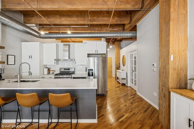 kitchen featuring a breakfast bar area, a sink, wall chimney range hood, appliances with stainless steel finishes, and decorative backsplash