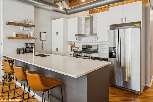 kitchen with a sink, a kitchen breakfast bar, appliances with stainless steel finishes, wall chimney range hood, and backsplash