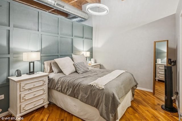 bedroom featuring baseboards, wood finished floors, and a decorative wall