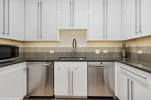 kitchen with appliances with stainless steel finishes, dark countertops, white cabinets, and a sink