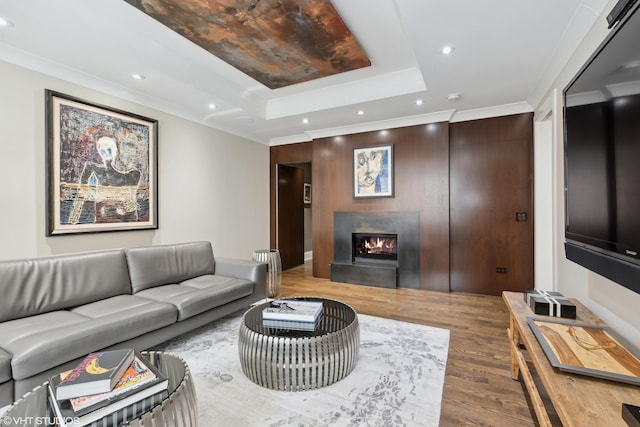 living area with ornamental molding, wood finished floors, a lit fireplace, a tray ceiling, and recessed lighting