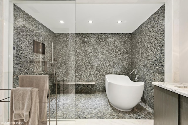 bathroom featuring a shower with shower door, recessed lighting, vanity, tile walls, and a freestanding bath