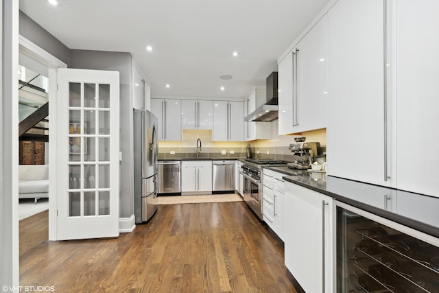 kitchen featuring wine cooler, dark countertops, appliances with stainless steel finishes, white cabinets, and wall chimney range hood