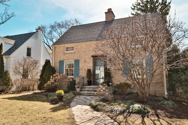 view of front facade featuring a shingled roof, brick siding, and a chimney