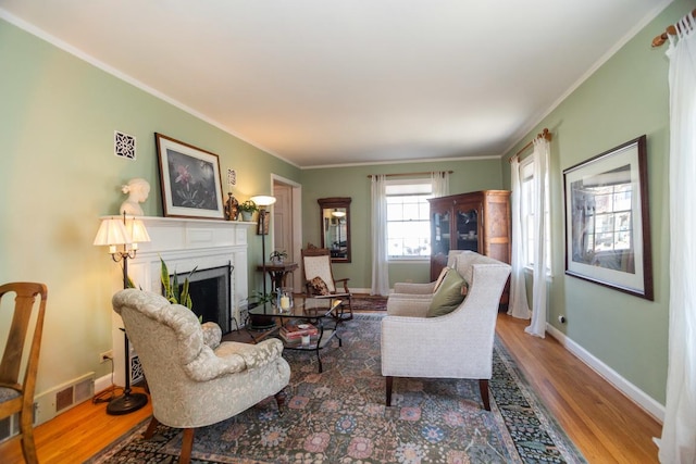 living area featuring visible vents, wood finished floors, a fireplace, crown molding, and baseboards