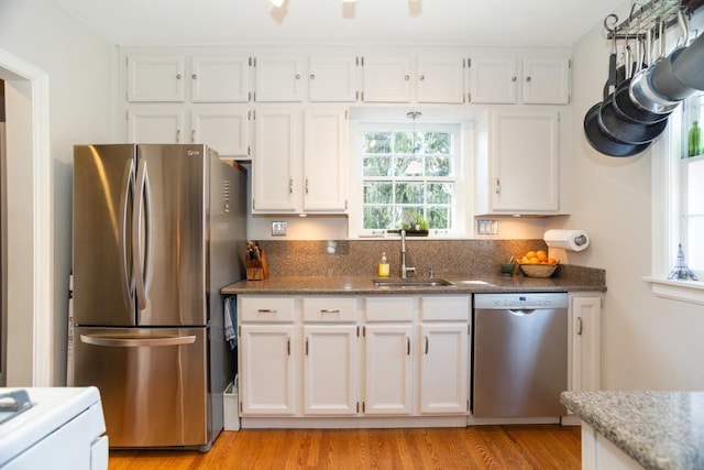 kitchen with dark stone countertops, light wood-style flooring, a sink, white cabinets, and appliances with stainless steel finishes