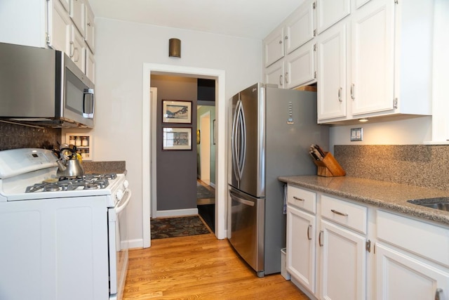 kitchen with white cabinets, stainless steel appliances, light wood-type flooring, and baseboards